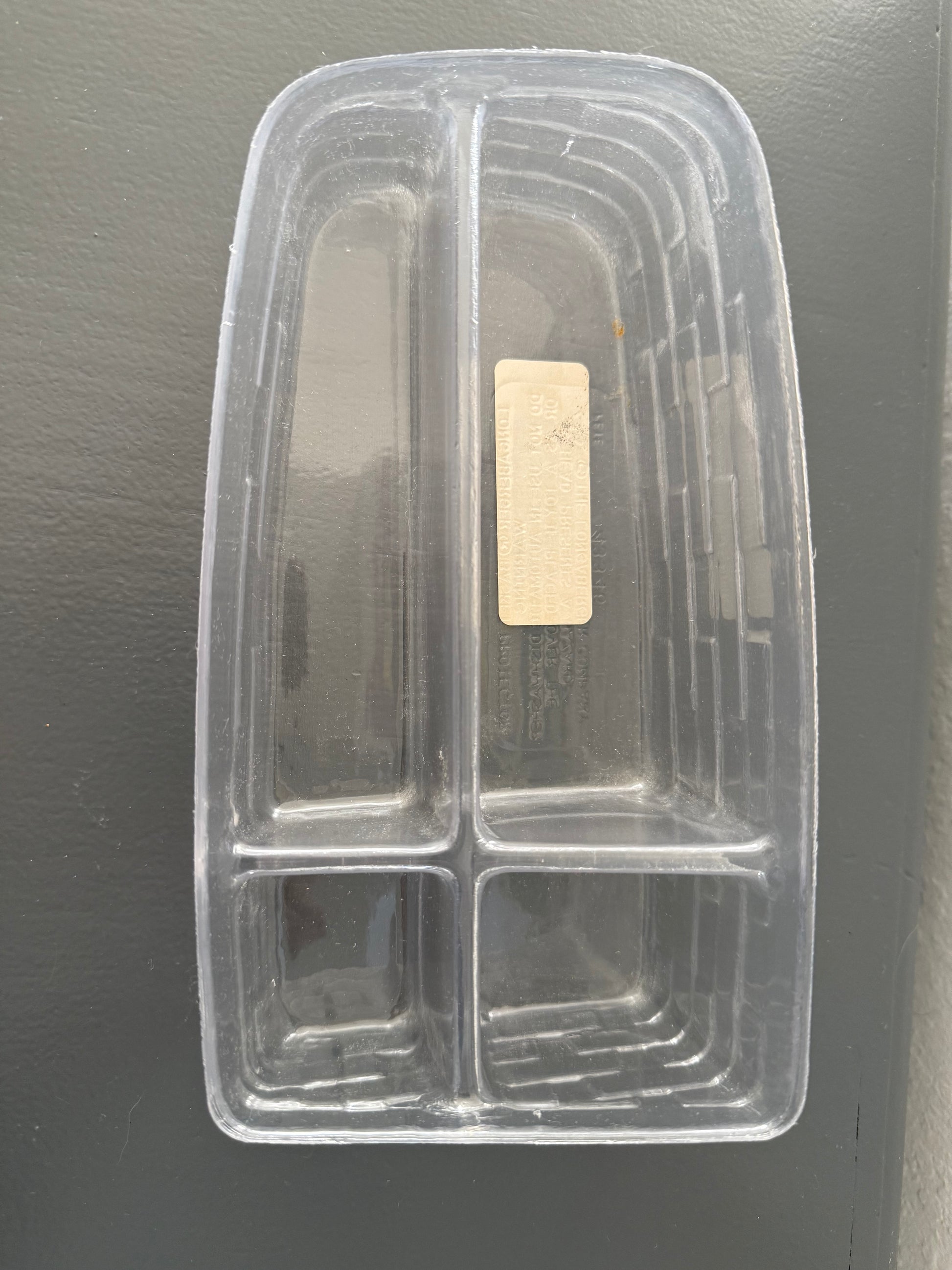 Clear plastic compartmentalized tray with a gold label on a gray background