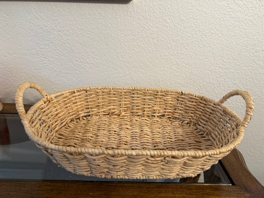 Woven basket with handles on a wooden surface against a white wall