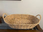 Woven basket with handles on a wooden surface against a white wall