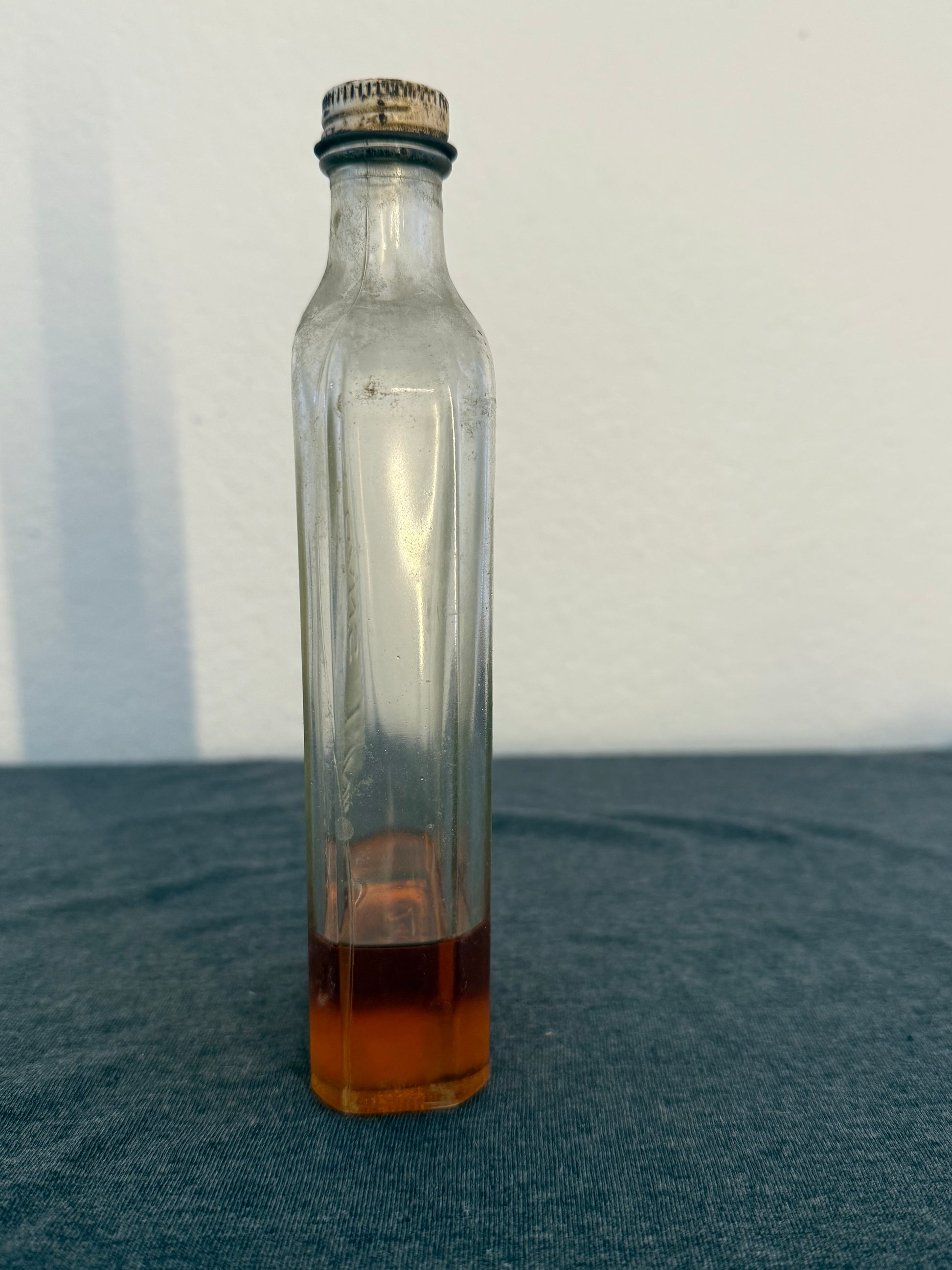 Clear glass bottle with a dark brown liquid on a white and gray background