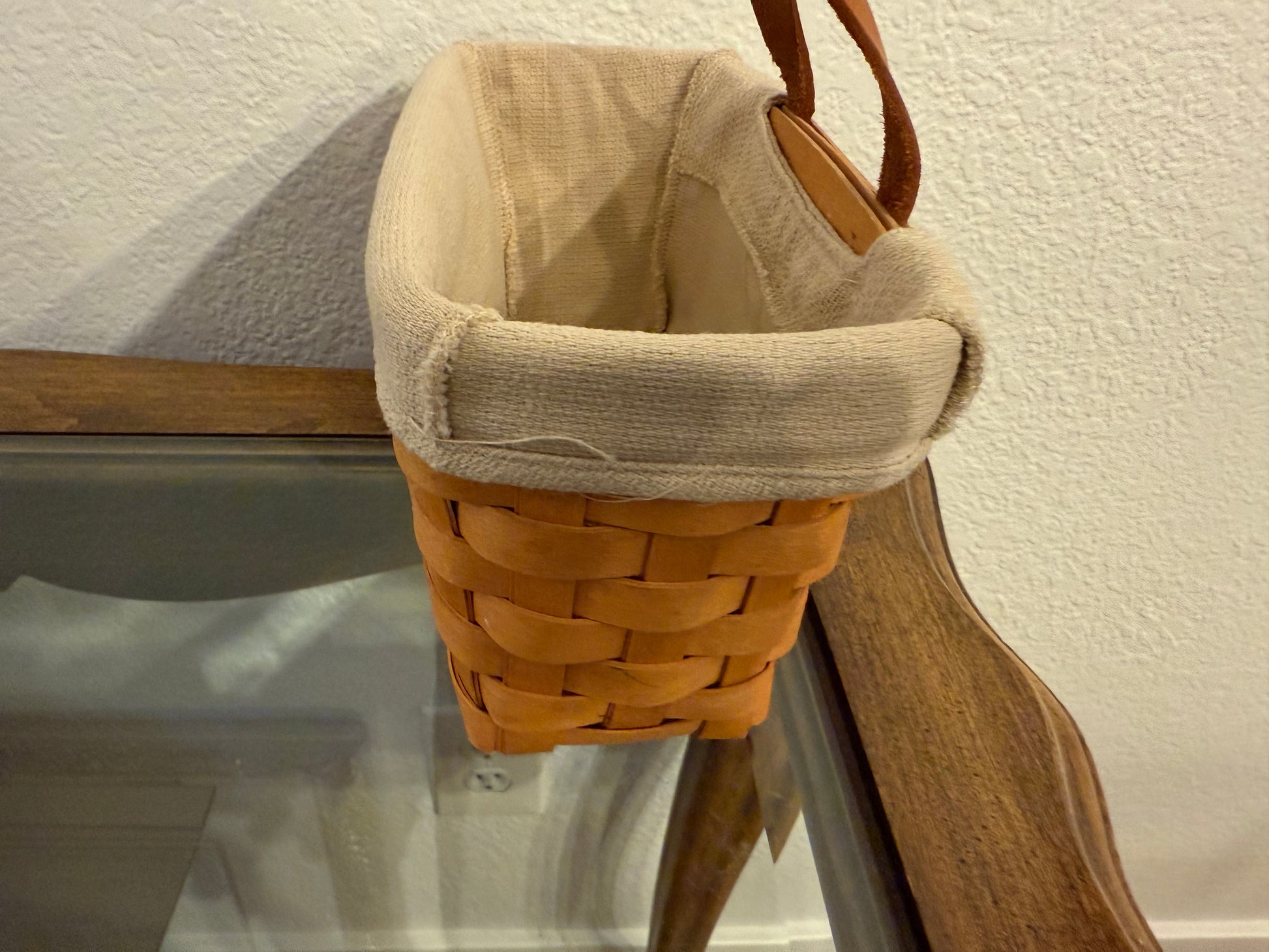 Woven basket with a beige liner hanging on a wooden surface.