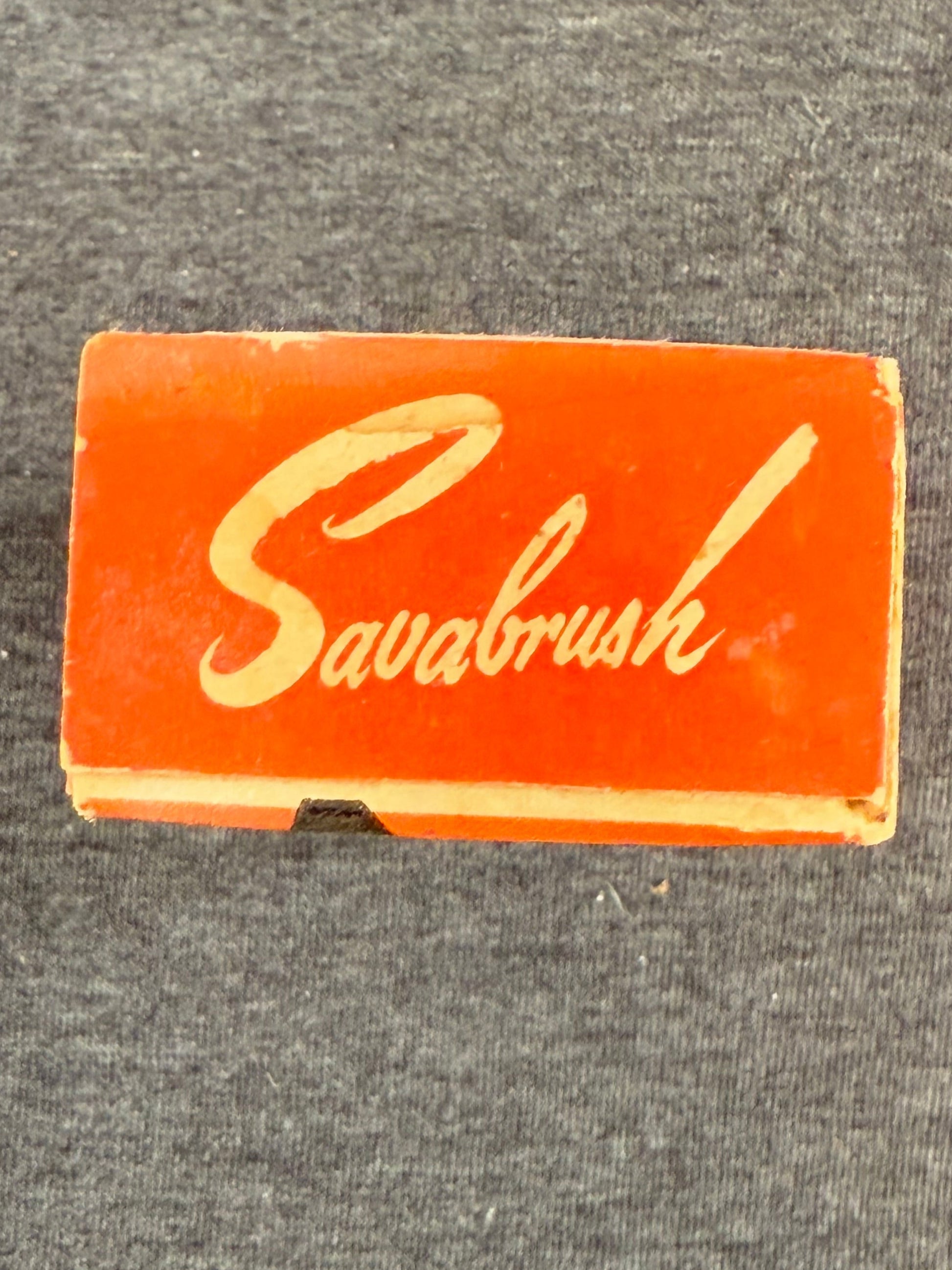 Small red box with 'Savabrush' logo on a gray textured background