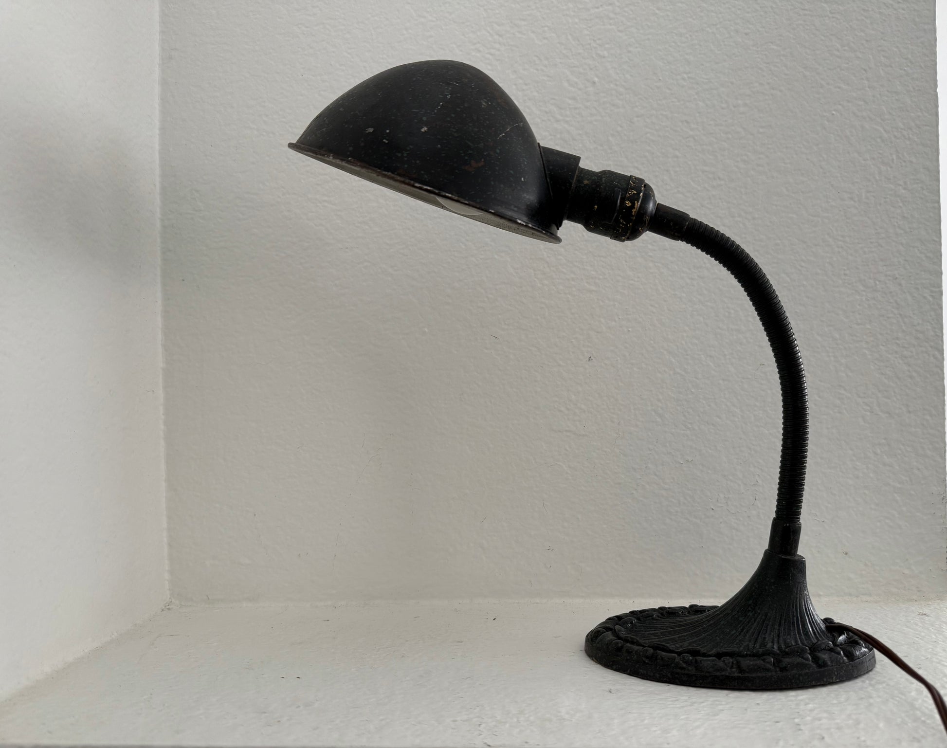 Black vintage-style desk lamp on a white surface with a light gray wall background