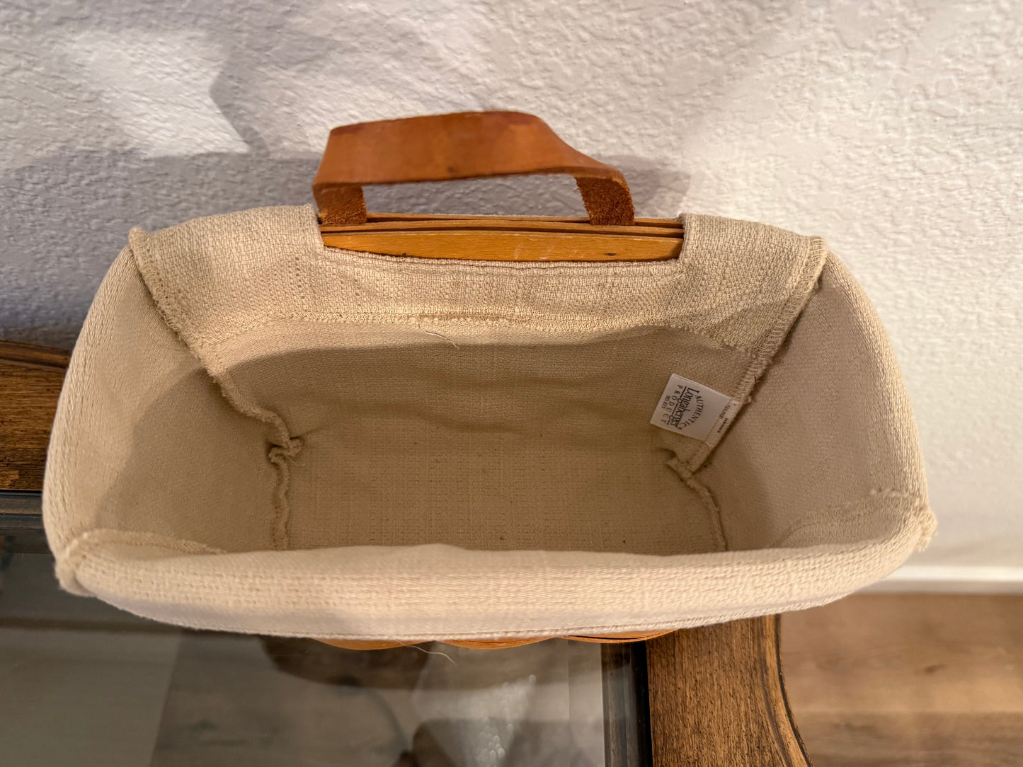 Beige fabric basket with a brown handle on a textured surface