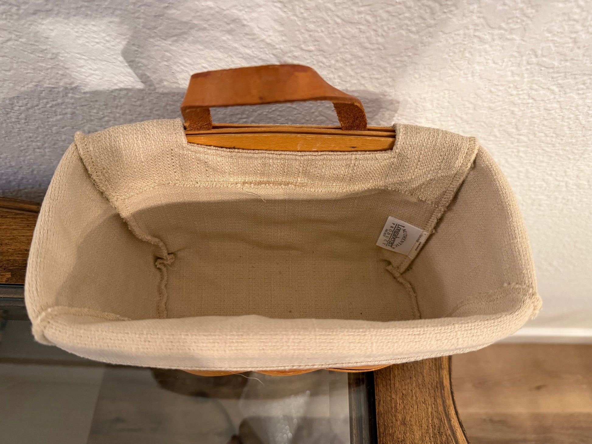 Beige fabric basket with a brown handle on a textured surface