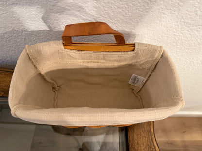 Beige fabric basket with a brown handle on a textured surface