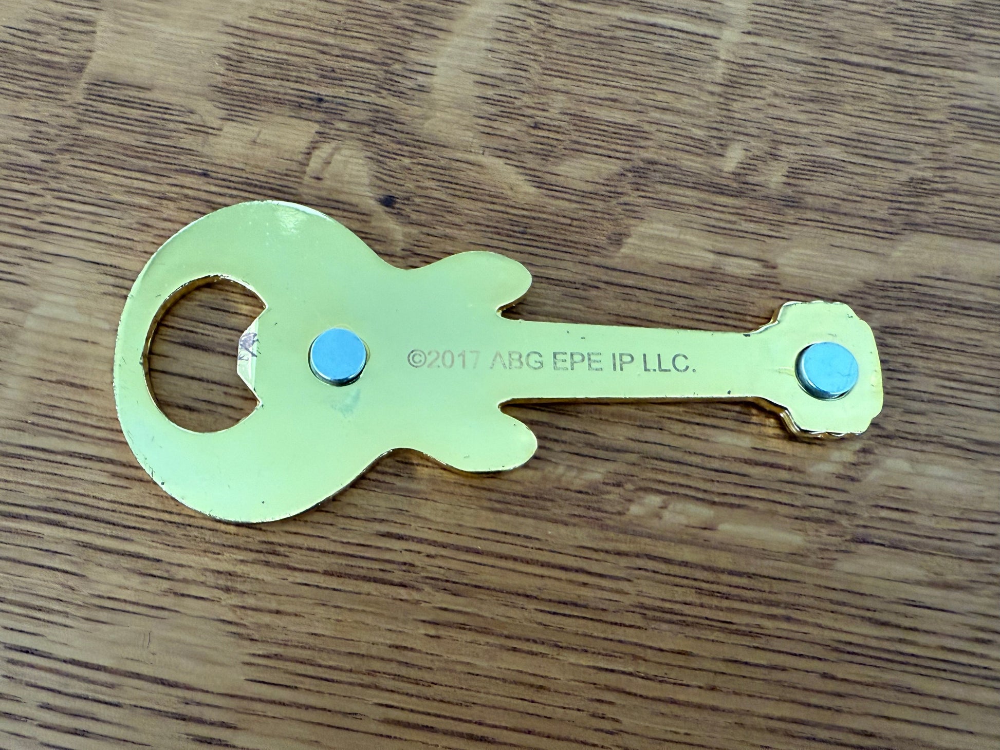 Metallic guitar-shaped bottle opener on a wooden surface