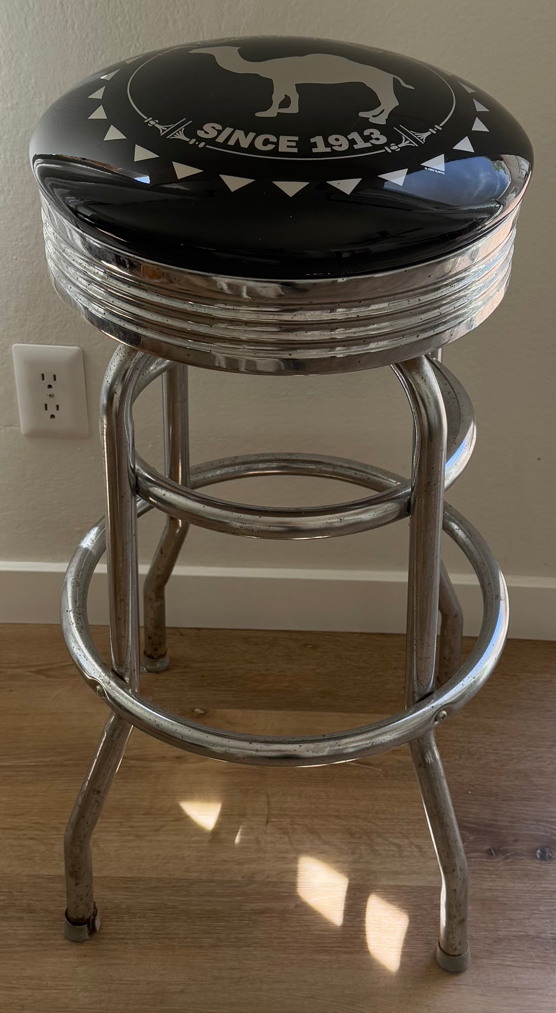 Bar stool with black cushion and metallic frame on a wooden floor.