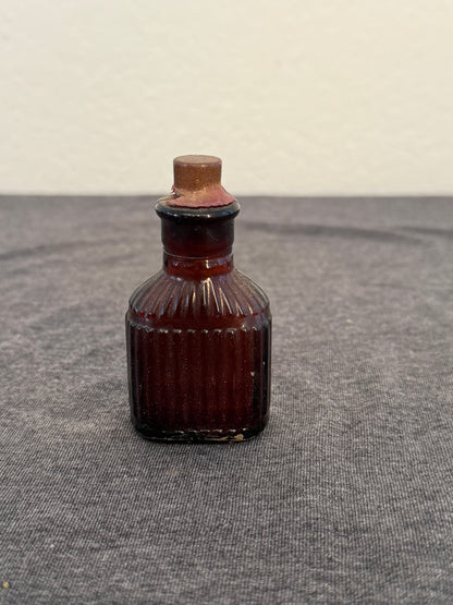 Small brown glass bottle with a ribbed design on a gray surface
