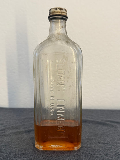 Vintage glass bottle labeled 'Sloan's Liniment' on a gray background
