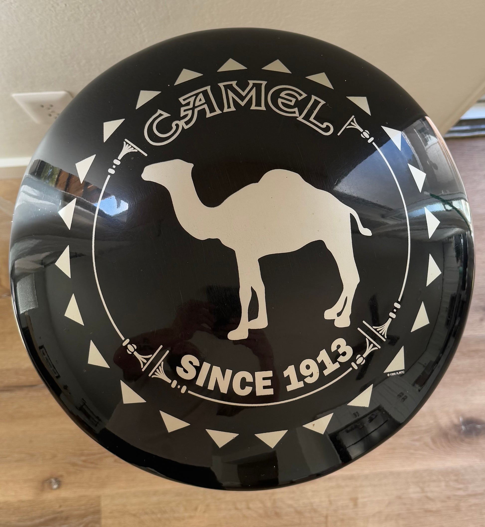 Round black sign with white camel and text on a wooden surface