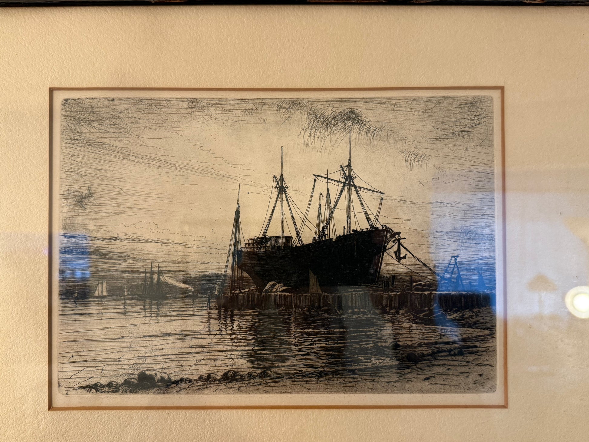 Framed black and white drawing of a ship on water with a beige wall background