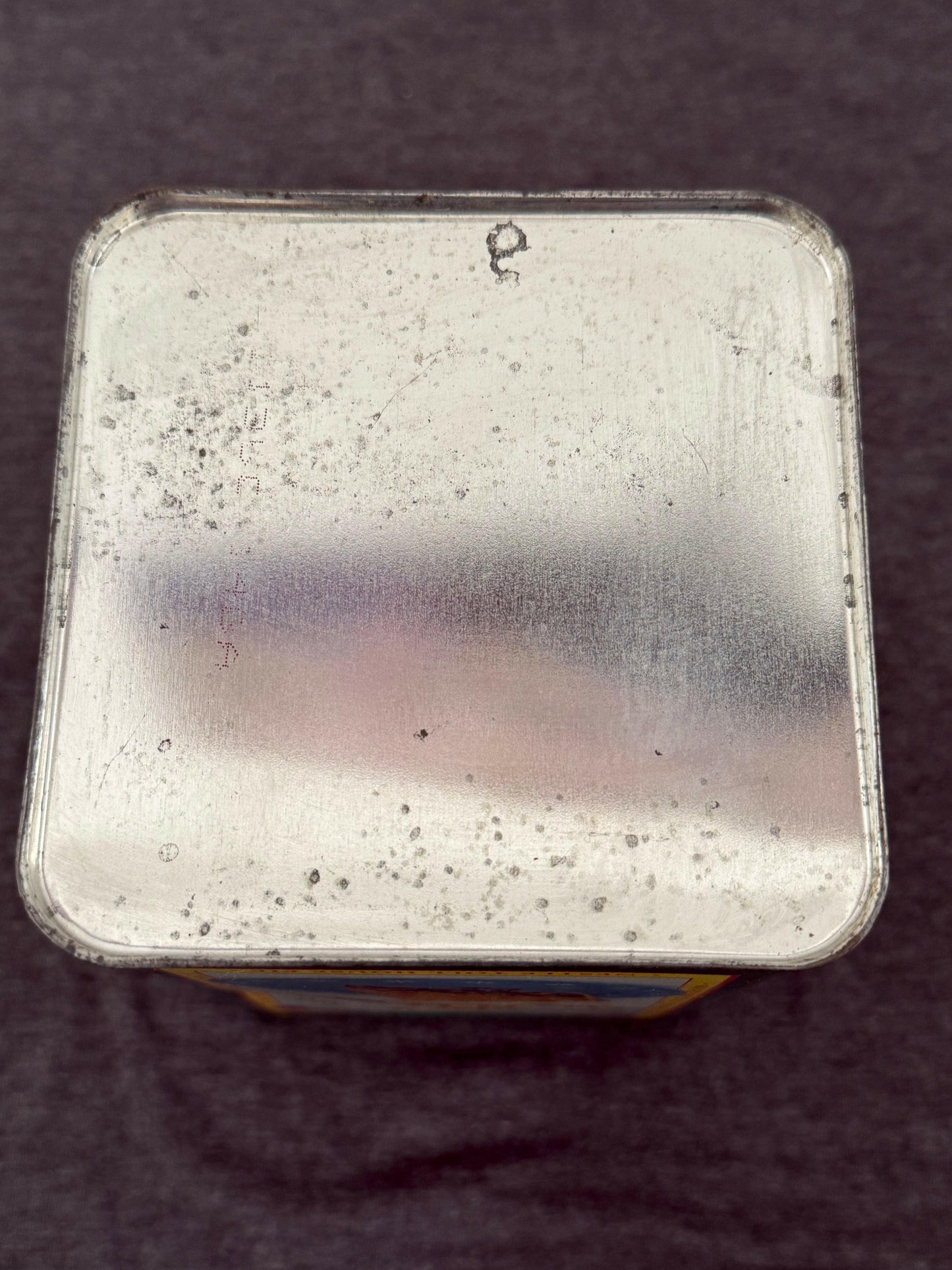 Metallic square object with speckled texture on a dark background