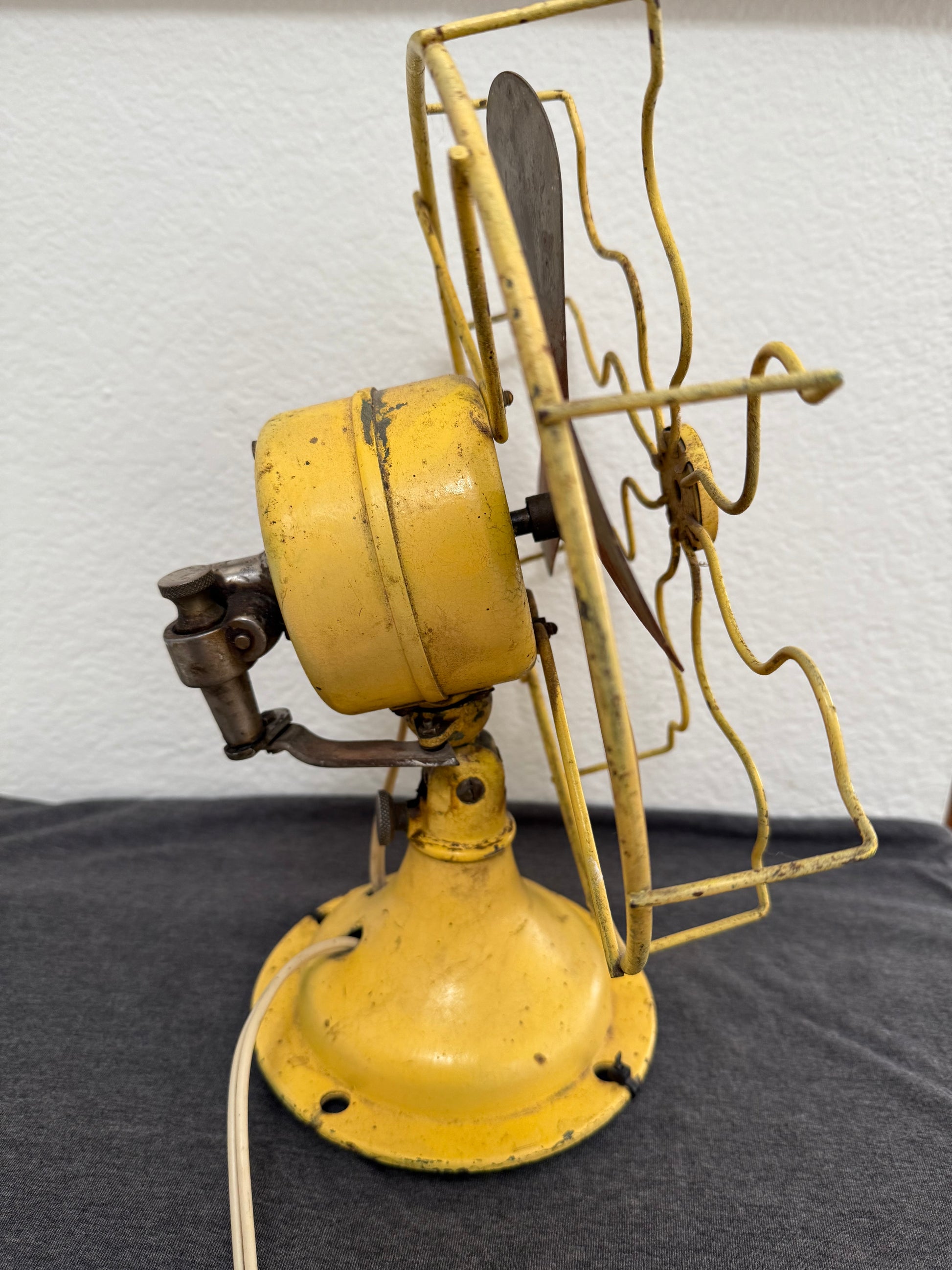 Vintage yellow fan with metal blades against a white wall.