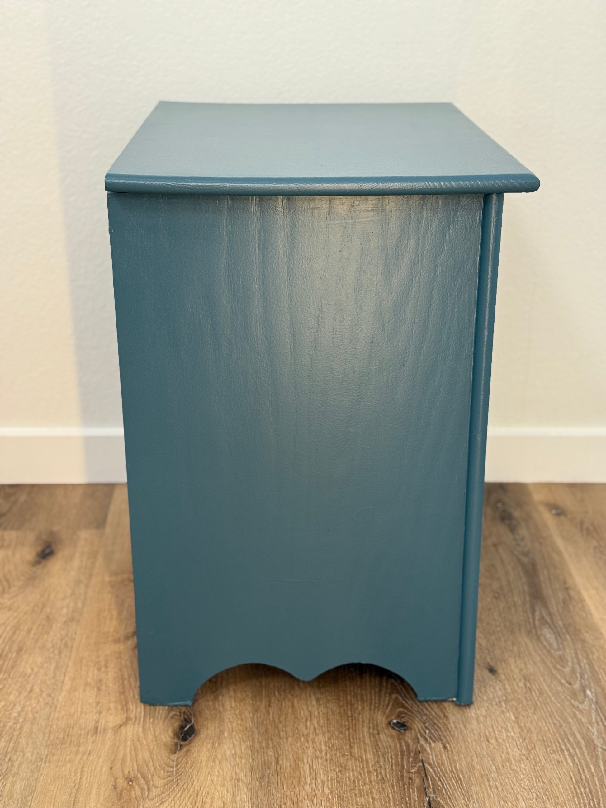 Blue wooden side table on a wooden floor with a white wall background