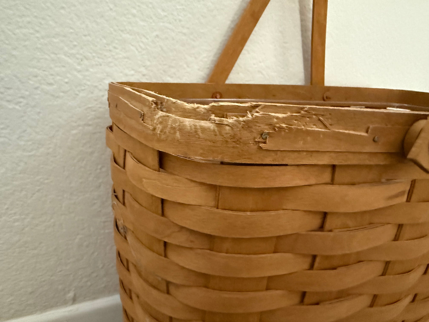 Woven brown basket with a handle against a white wall
