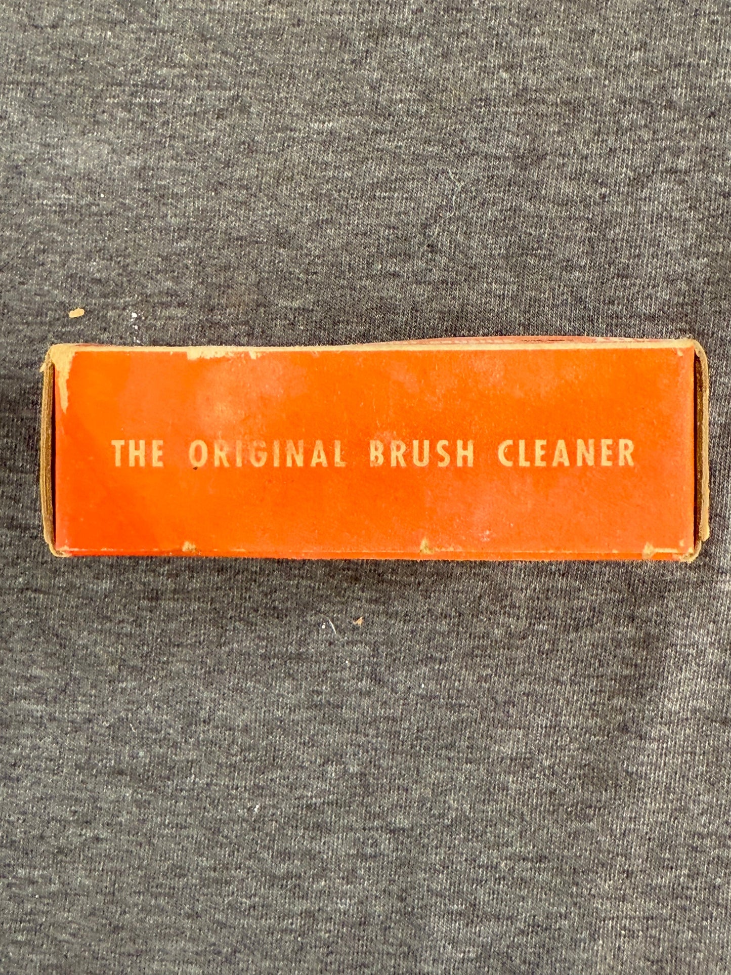 Vintage orange box labeled 'The Original Brush Cleaner' on a gray textured background