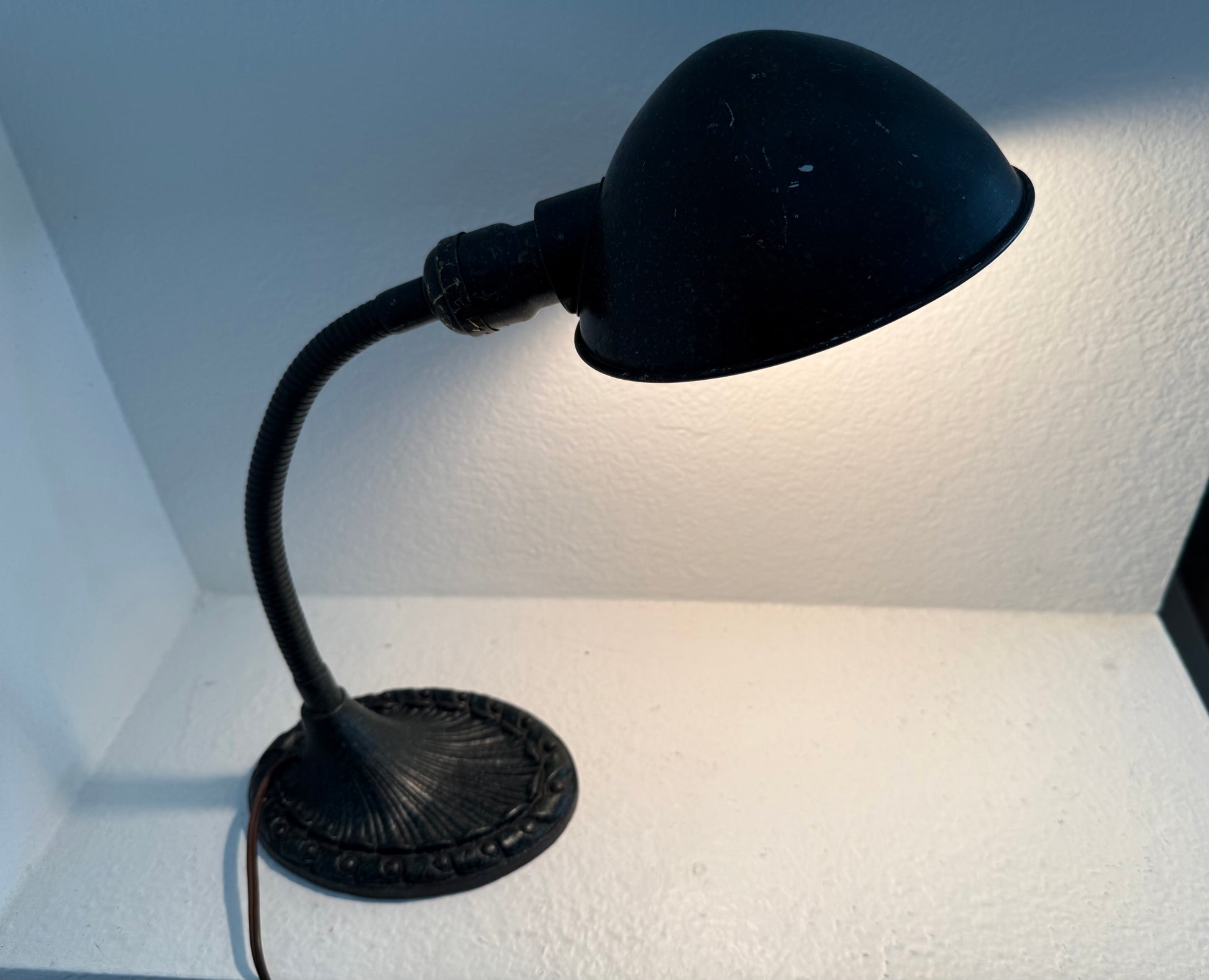 Black adjustable desk lamp on a textured white surface with a light blue wall background