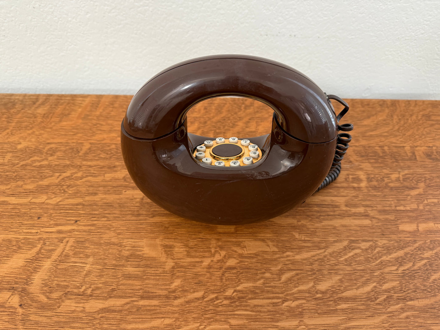 Brown rotary phone on a wooden surface with a white wall background