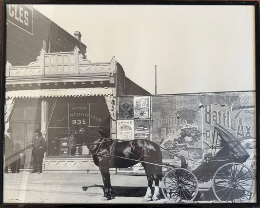 Black and white photo with a horse drawn carriage in front of advertisements