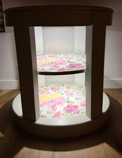 Oval side table with floral-patterned cushion on a wooden floor.