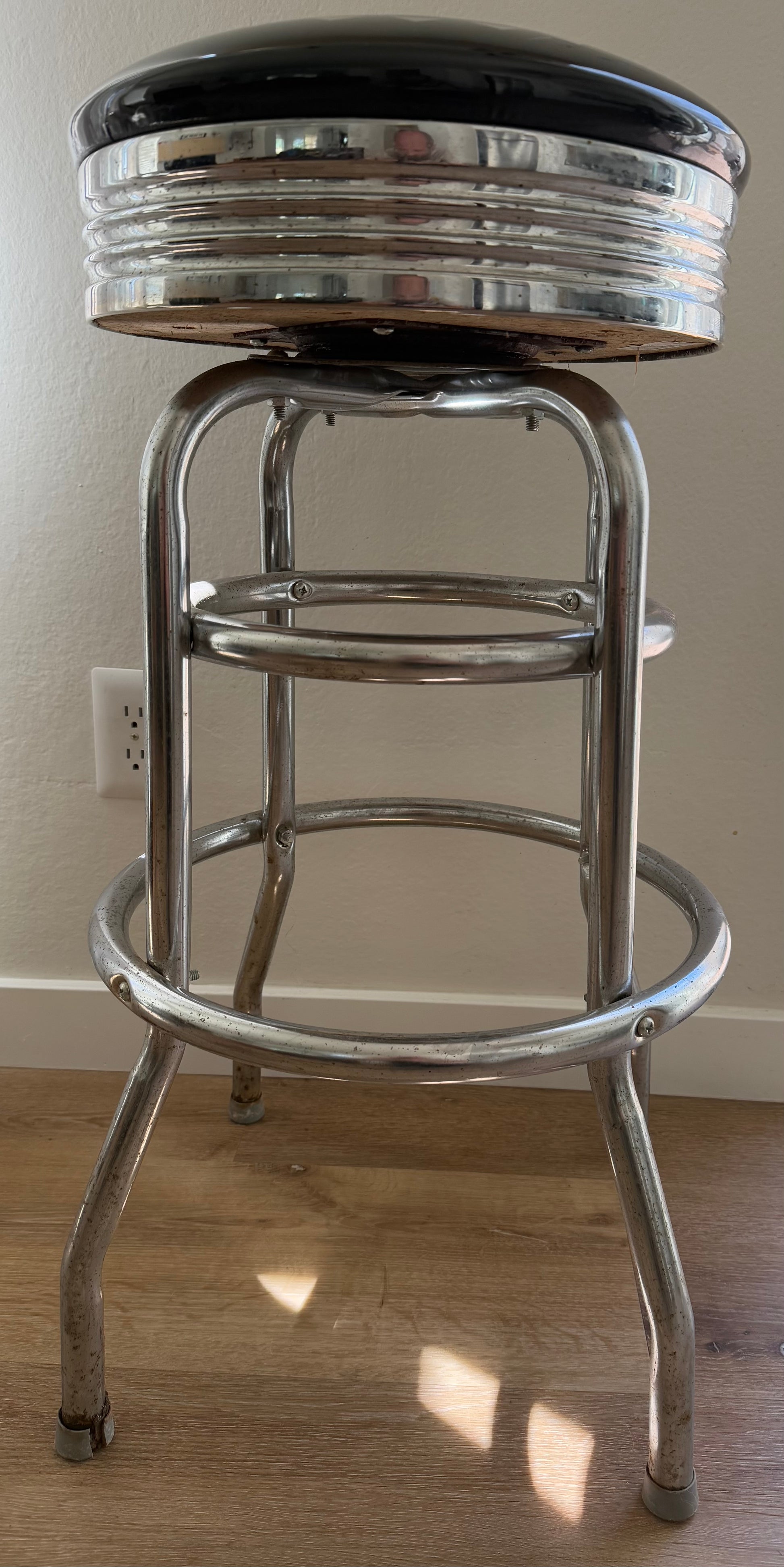 Bar stool with black cushioned seat and chrome frame on a wooden floor.