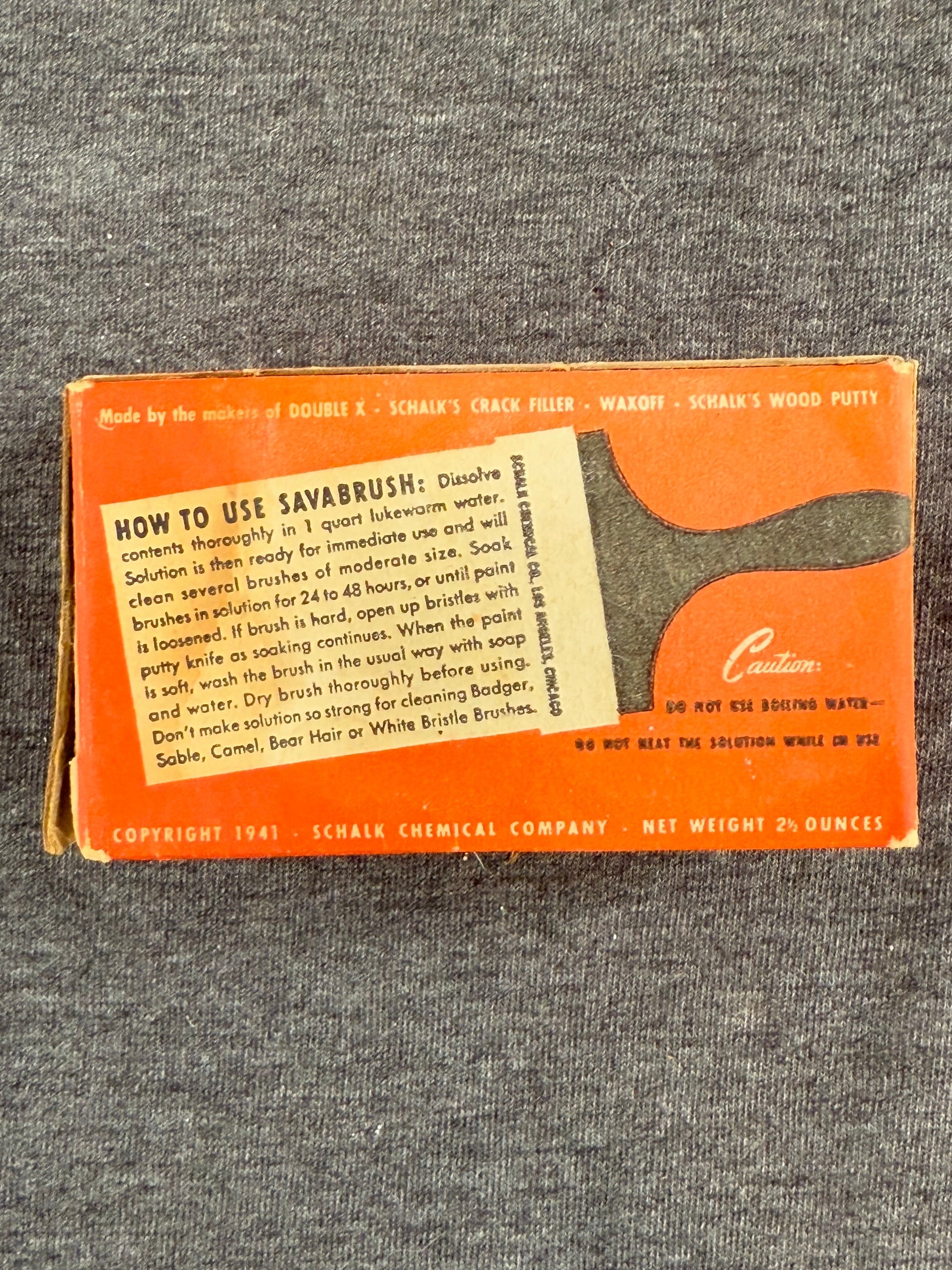 Vintage box with a brush illustration and text on an orange background, placed on a textured gray surface.
