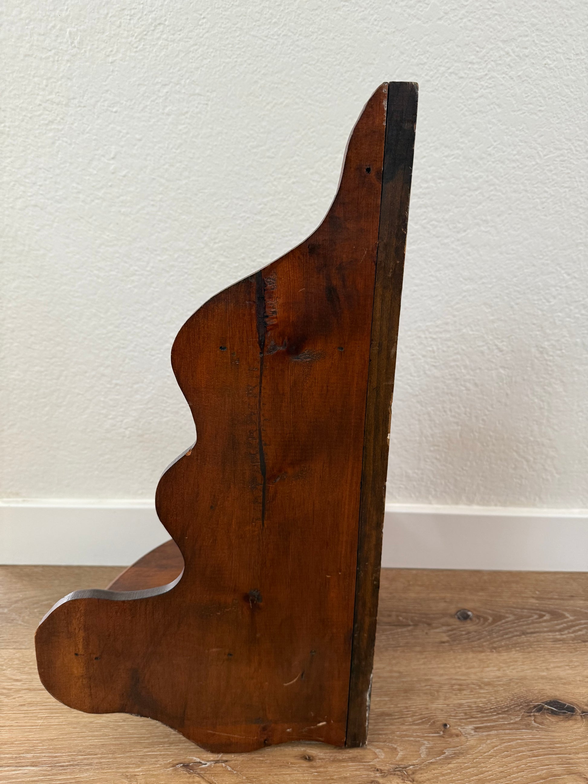 Wooden shelf sitting on a wood floor with white wall in the background.