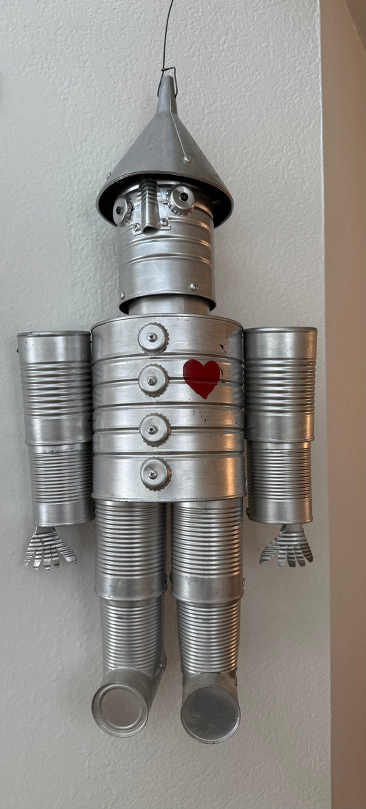 Metal tin man sculpture with a heart on its chest against a plain wall