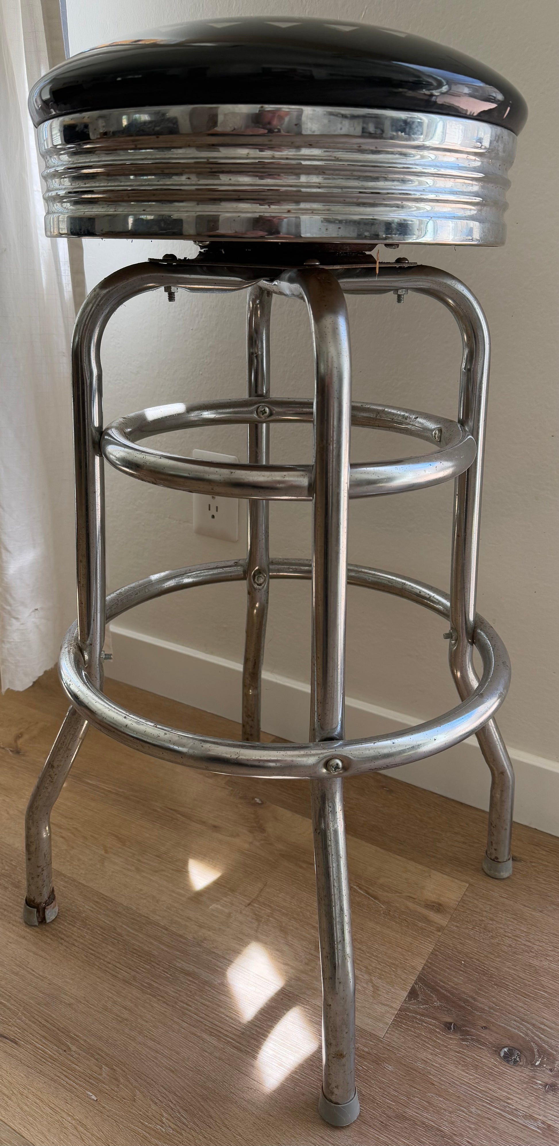 Vintage-style bar stool with metal frame and black cushioned seat on a wooden floor.