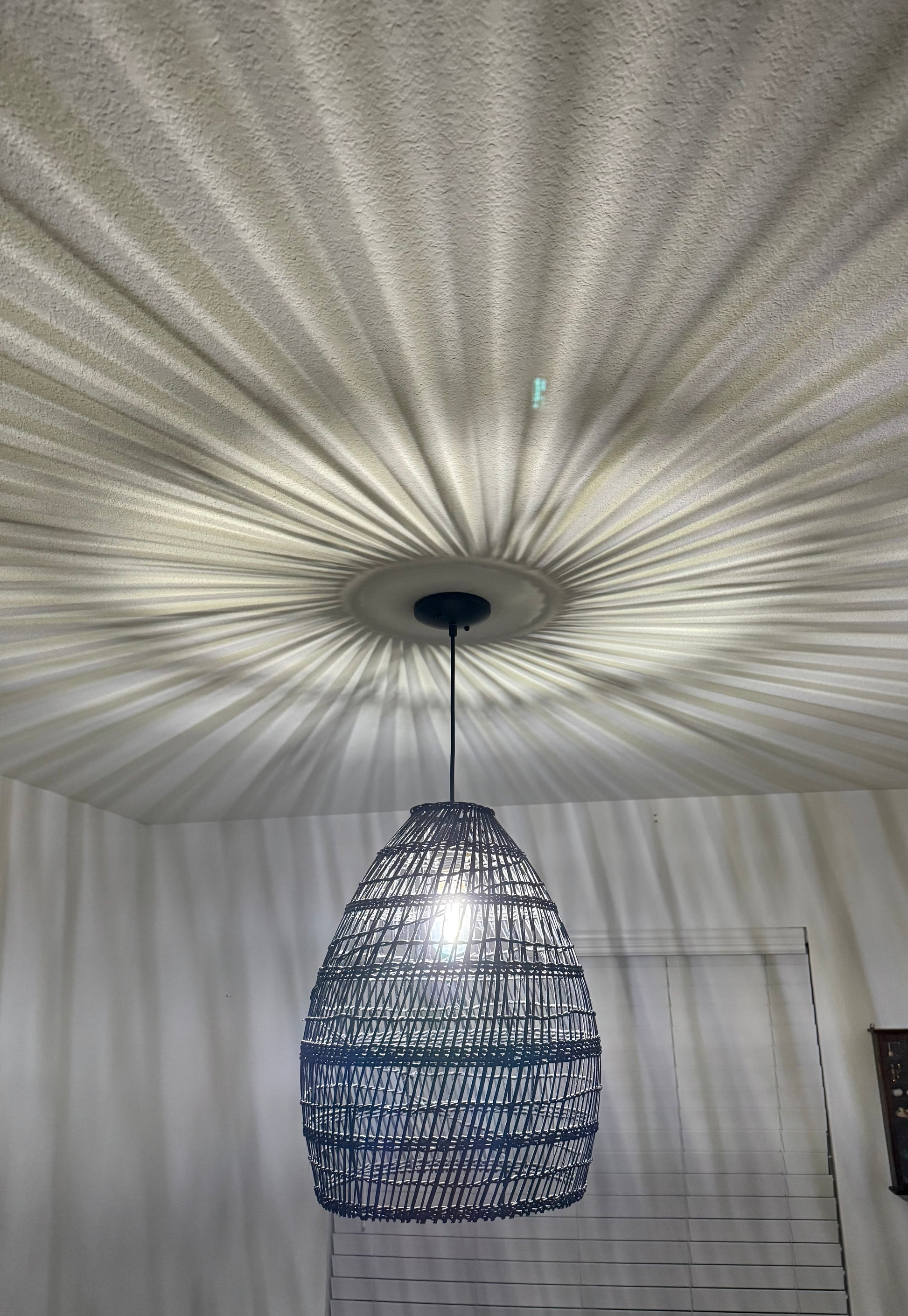 Woven pendant light fixture hanging from a textured ceiling