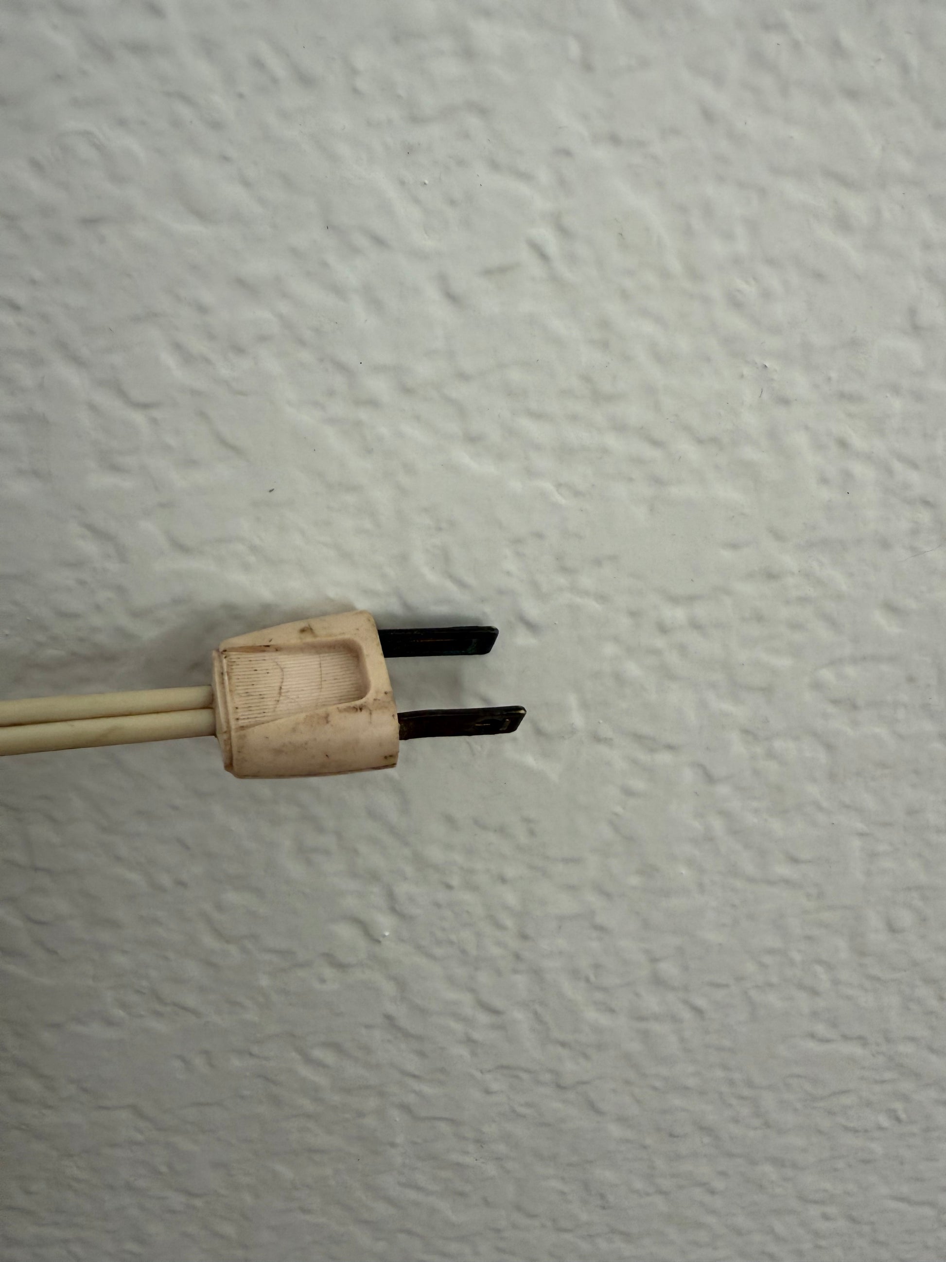 Old-style electrical plug against a textured white wall