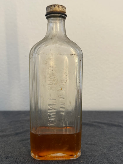 Clear glass bottle with brown liquid on a light gray background