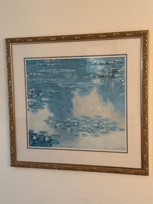 Framed reproduction of Monet's Water Lillies artwork with abstract blue design on a beige wall