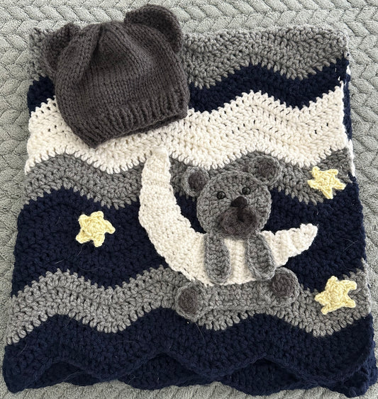 Crocheted blanket with bear design, stars, and matching hat on a textured surface.