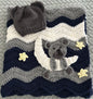 Crocheted blanket with bear design, stars, and matching hat on a textured surface.