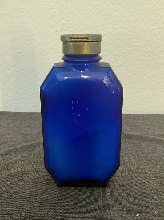 Cobalt blue glass bottle with a metallic cap on a gray and white background