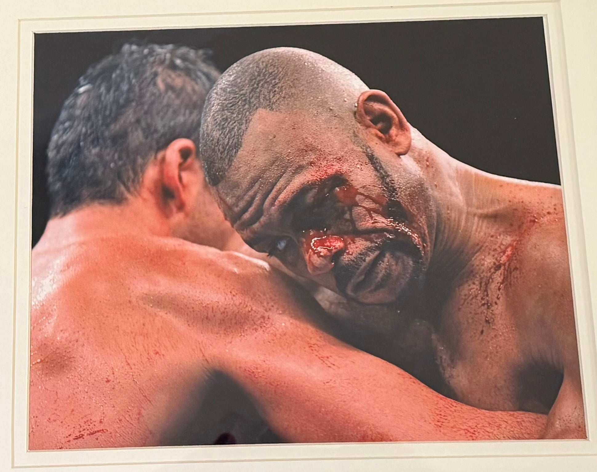 Two muscular men facing each other with one showing signs of injury.