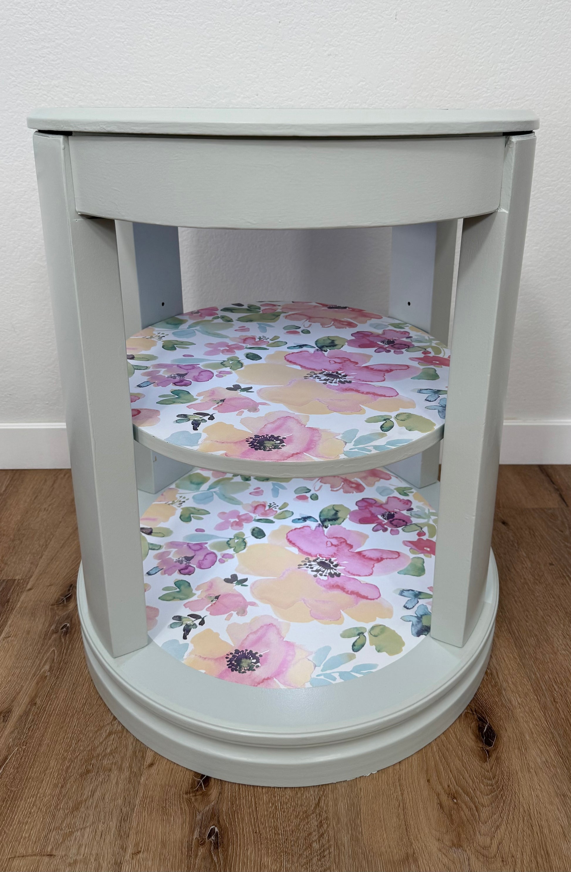 Round gray table with floral-patterned shelves on a wooden floor.