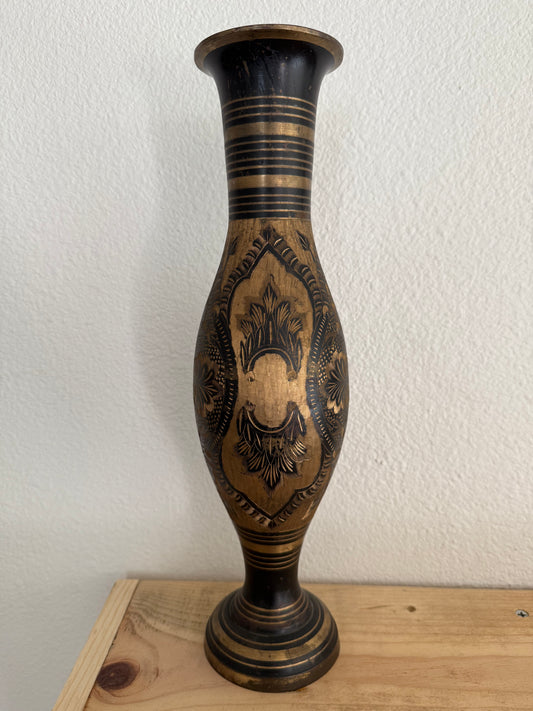 Decorative brass vase with intricate carvings on a white wall.