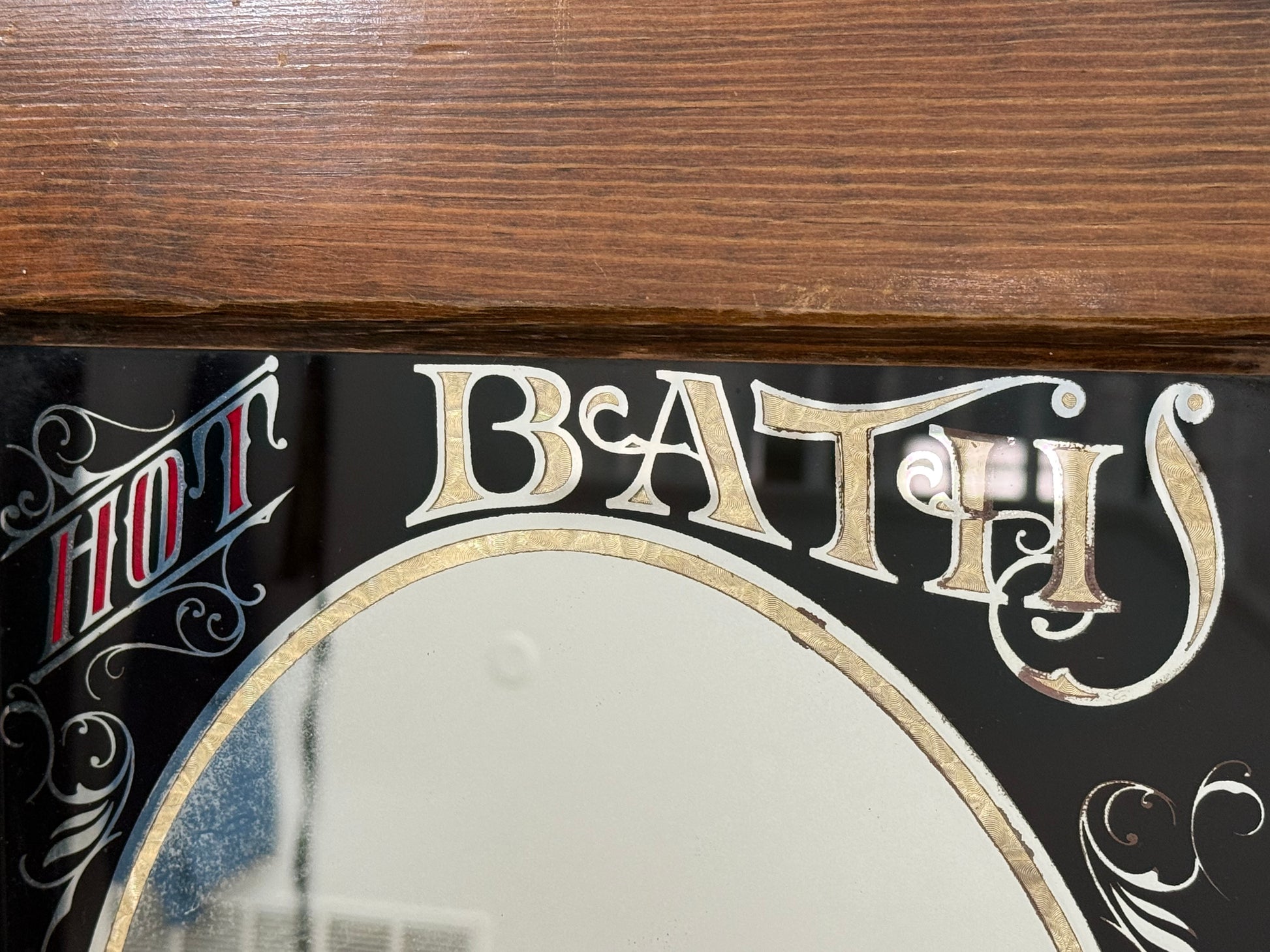 Decorative mirror with 'HOT BATH' text on a wooden surface