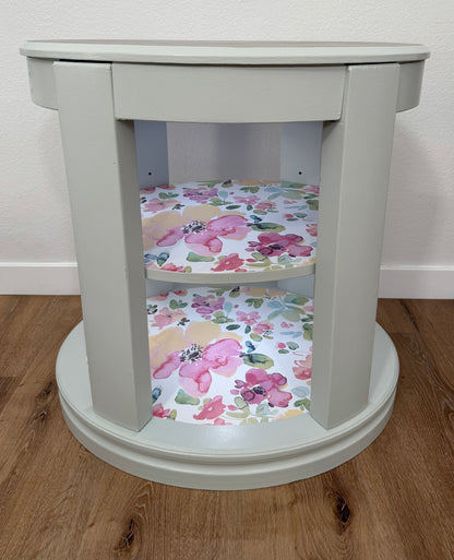 Oval side table with floral-patterned shelves on a wooden floor.