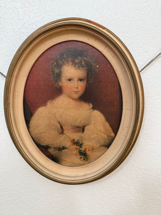 Vintage oval portrait of a child in a gold frame on a textured white wall.
