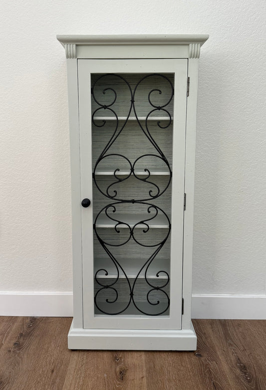White cabinet with decorative wrought iron door on a wooden floor and white wall background