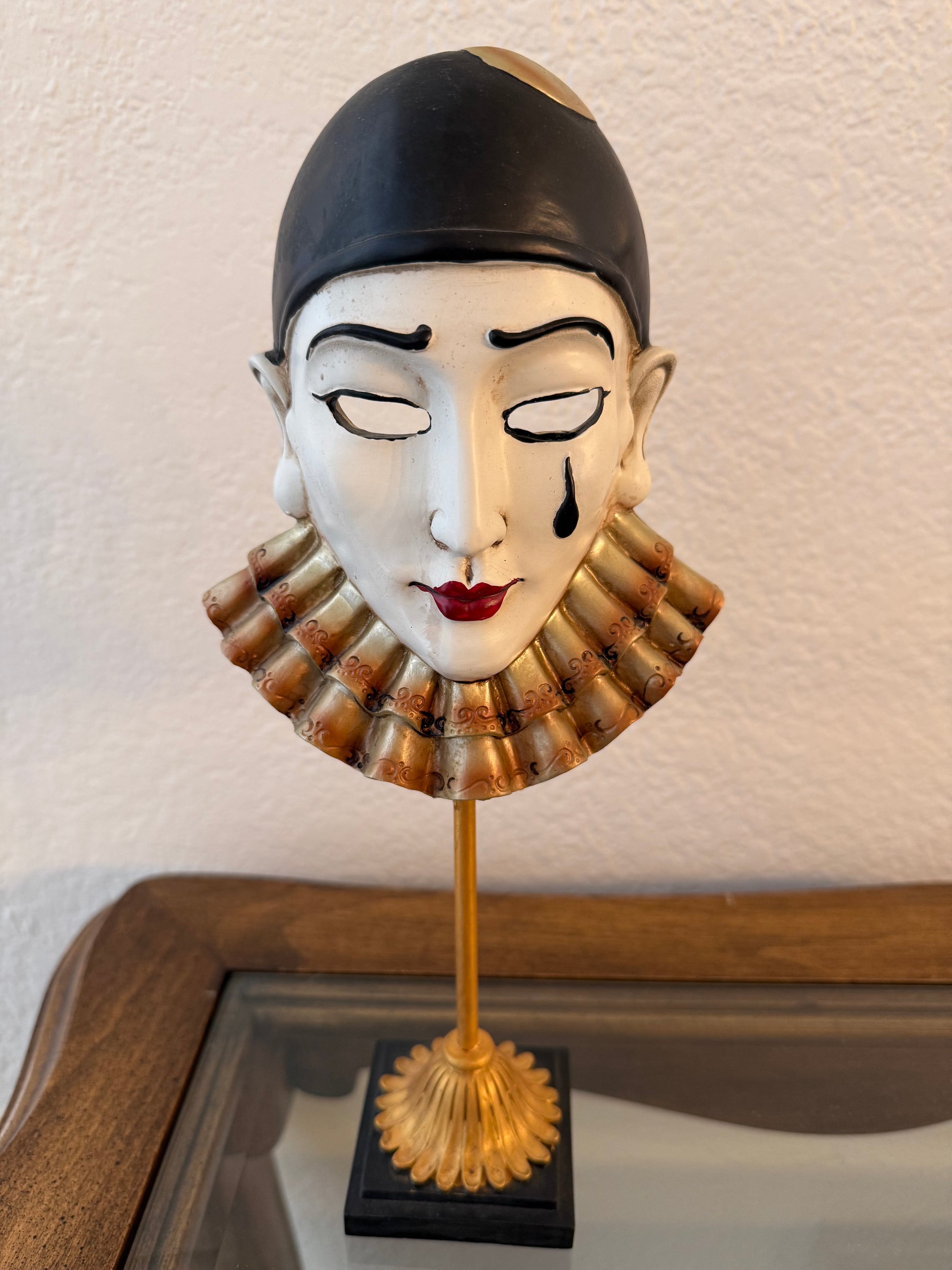 Decorative wall mask with black hair and red lips on a white wall.