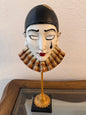 Decorative wall mask with black hair and red lips on a white wall.